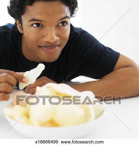 Close-up of a young man taking a <b>prawn cracker</b> from a bowl - x18666499