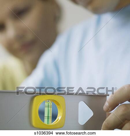 Man using level tool with woman in background, focus on level and hand, close-up - s1036394