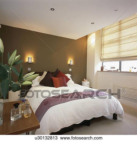 Stock Photo of Wall-lights on brown wall above bed with white duvet in modern bedroom with cream ...