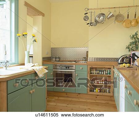 Stock Image Of Green Ed Units In Modern Pastel Yellow Kitchen Green Ed Units In Modern Pastel Yellow Kitchen With Saucepans On Hanging Wall Rack
