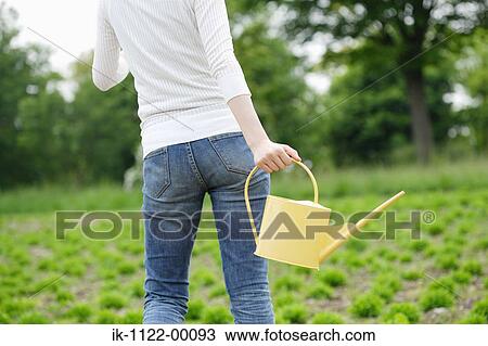 Stock Image - A woman holding watering can in garden. Fotosearch
