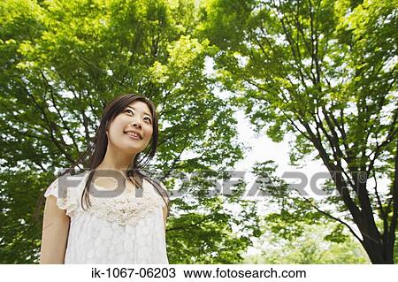 Stock Image - A young smiling woman standing in park. Fotosearch