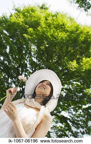 A young woman holding flower looking at sky View Large Photo Image Stock Photograph - A young woman holding flower looking at sky. Fotosearch