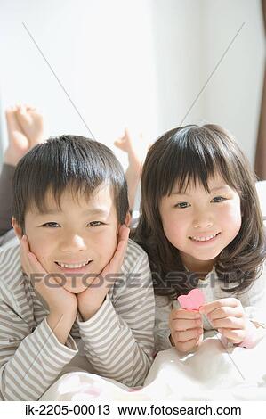 Stock Image - Asian children lying on a bed. Fotosearch