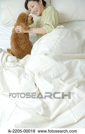 Stock Photo - Asian woman with her pet dog on bed. Fotosearch
