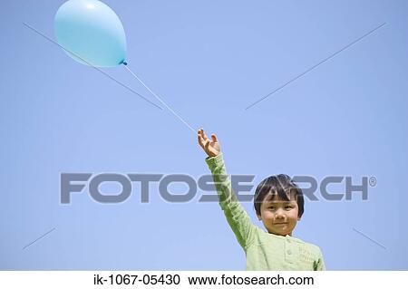 Stock Image - Boy holding balloon against blue sky. Fotosearch