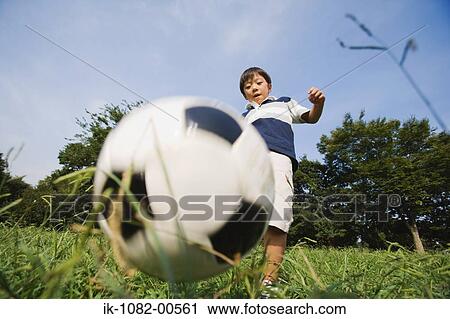 Stock Image - Boy playing with football in park. Fotosearch