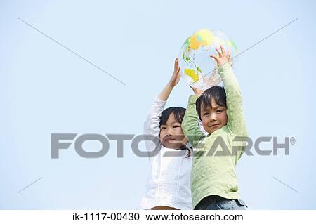 Stock Image - Children holding ball against blue sky. Fotosearch