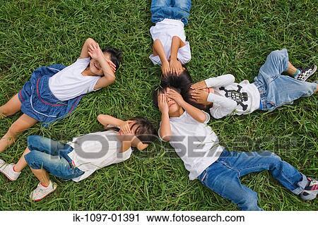 Children lying on grass hiding their faces View Large Photo Image Stock Image - Children lying on grass hiding their faces. Fotosearch