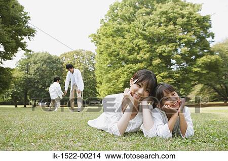 Family Laying Down on Grass; Father and Son in Background View Large Photo Image Picture - Family Laying Down on Grass; Father and Son in Background. Fotosearch