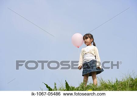 Stock Photograph - Girl holding balloon against blue sky. Fotosearch