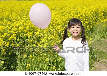 Stock Image - Girl holding balloon in mustard flowers. Fotosearch