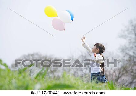 Stock Image - Girl holding colorful balloons in park. Fotosearch