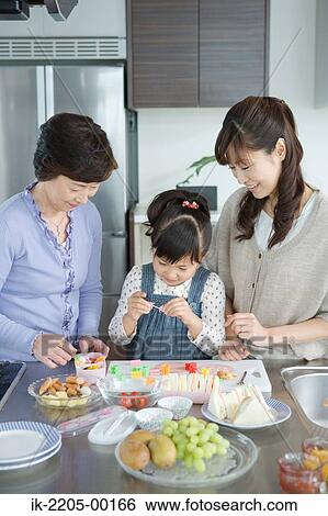 Stock Photograph - Girl preparing breakfast with her mother and grandmother. Fotosearch