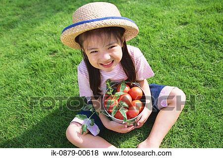 Stock Photo - Girl sitting on grass holding bucket of tomatoes. Fotosearch