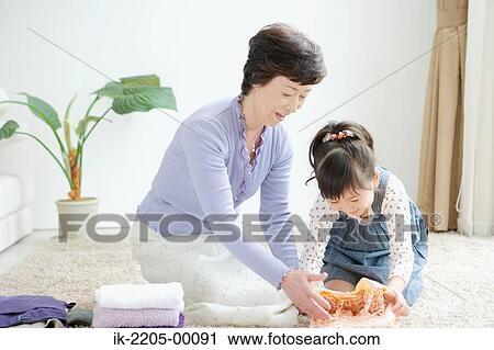 Stock Image - Girl with grandma folding clothes. Fotosearch