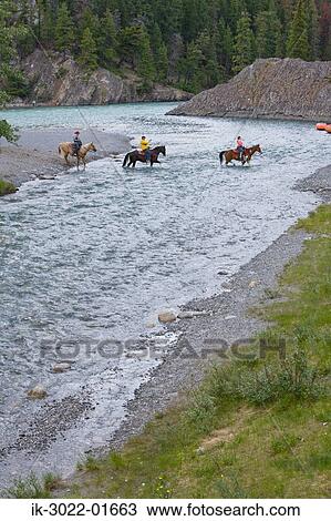 Stock Image - Horse Riders Crossing River in Banff, Canada. Fotosearch