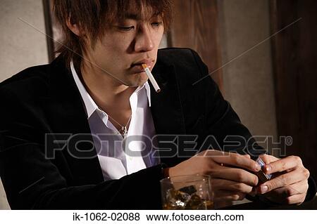 Stock Photo - Japanese man handling a carton of cigs with unlit cigarette on lips. Fotosearch