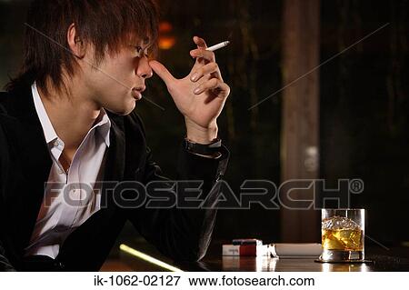 Stock Photo - Japanese Man in bar thinking w/ cigarette and scotch-whiskey. Fotosearch