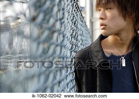 Stock Image - Japanese man looking beyond the chain-link fence. Fotosearch