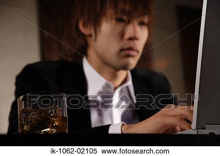 Stock Photography - Japanese man out of focus with scotch-whiskey and laptop in focus. Fotosearch