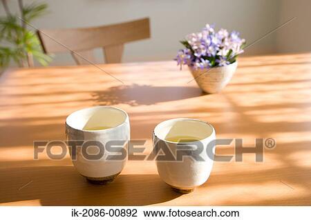 Stock Image - Japanese Tea on Table with Flower Vase in Background . Fotosearch