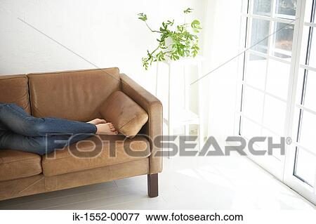 Low section of a person lying on sofa in living room View Large Photo Image Stock Photo - Low section of a person lying on sofa in living room. Fotosearch
