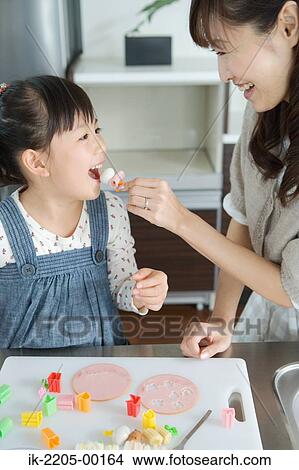 Picture - Mother feeding snacks to his daughter. Fotosearch