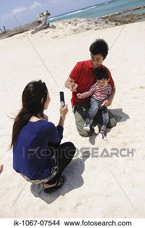 Mother taking snap of her family on beach View Large Photo Image Picture - Mother taking snap of her family on beach. Fotosearch