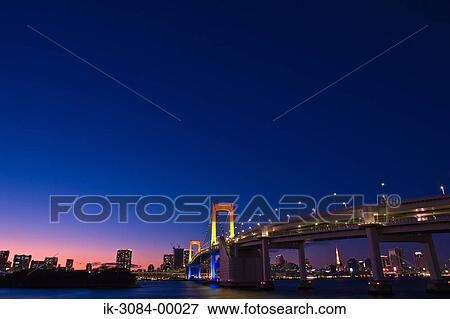 Stock Photo - Rainbow bridge with buildings and illuminated lights in nighttime. Fotosearch