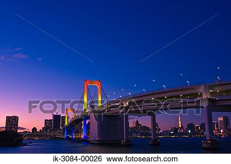 Stock Photograph - Rainbow bridge with buildings and illuminated lights. Fotosearch