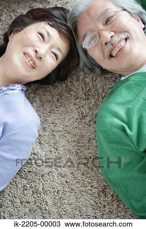 Stock Image - Senior couple lying head to head on carpet. Fotosearch