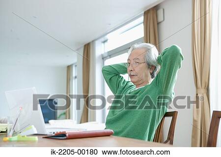 Stock Image - Senior man with hands behind head sitting at table. Fotosearch