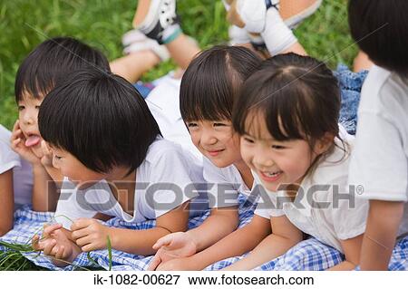 Stock Photo - Smiling children lying on front together in park. Fotosearch