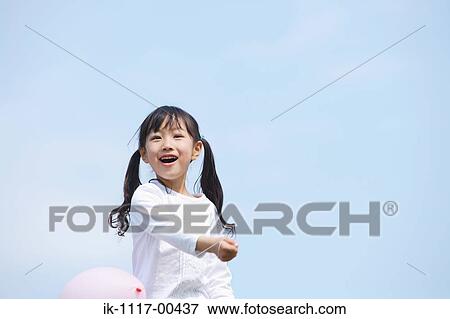 Smiling girl playing with balloon against blue sky View Large Photo Image Stock Photo - Smiling girl playing with balloon against blue sky. Fotosearch
