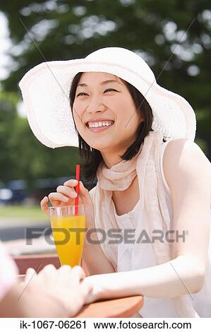 Stock Image - Smiling young woman having orange juice with straw. Fotosearch