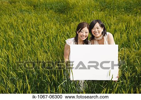 Stock Image - Smiling young women holding board in wheat field. Fotosearch