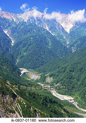 Stock Image - Snow-covered mountains with forest in wilderness. Fotosearch
