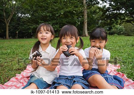 Stock Image - Three girls eating chocolate cake in a park. Fotosearch