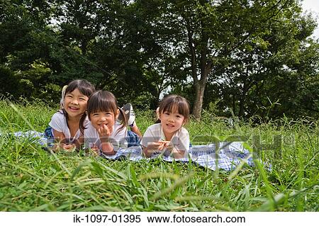 Stock Photography - Three girls lying on a grass in a row. Fotosearch