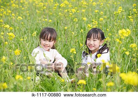 Stock Image - Two cute girls enjoying sitting together in mustard field. Fotosearch