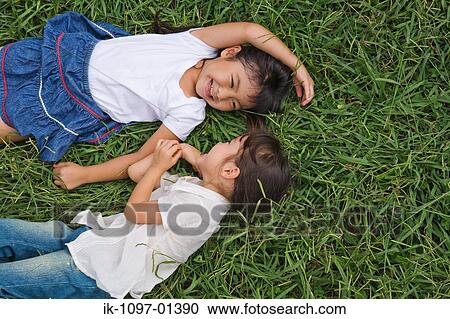 Stock Image - Two girls lying on grass in a park. Fotosearch