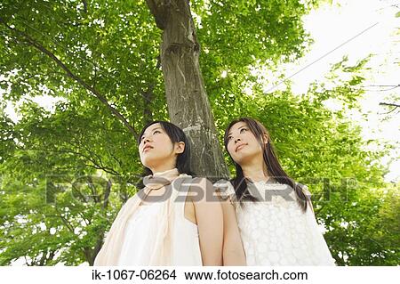 Picture - Two young sad women standing by tree. Fotosearch