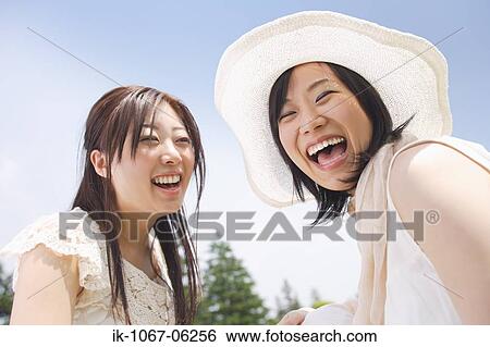 Two young smiling women sitting against blue sky View Large Photo Image Stock Photograph - Two young smiling women sitting against blue sky. Fotosearch