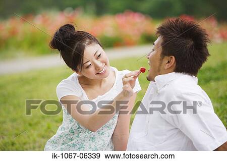 Stock Photo - Young Japanese couple feeding cherry. Fotosearch