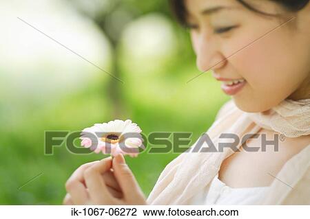 Stock Image - Young smiling woman holding flower. Fotosearch