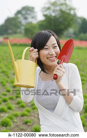 Young smiling woman holding shovel and watering can View Large Photo Image Stock Image - Young smiling woman holding shovel and watering can. Fotosearch