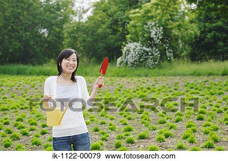 Young smiling woman holding trowel and watering can View Large Photo Image Stock Photo - Young smiling woman holding trowel and watering can. Fotosearch