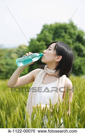 Young woman drinking water while standing in wheat field View Large Photo Image Stock Image - Young woman drinking water while standing in wheat field . Fotosearch
