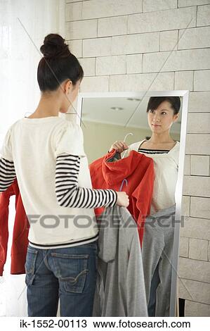 Stock Image - Young woman holding dress in front of mirror. Fotosearch